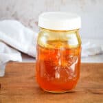 small mason jar filled with garlic infused honey on a wooden cutting board.
