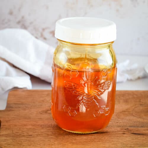 small mason jar filled with garlic infused honey on a wooden cutting board.