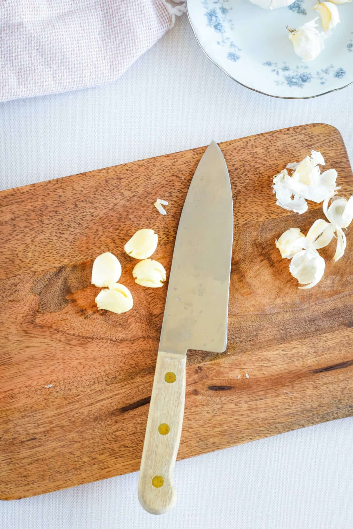 smashing and peeling garlic cloves with a knife on a cutting board.