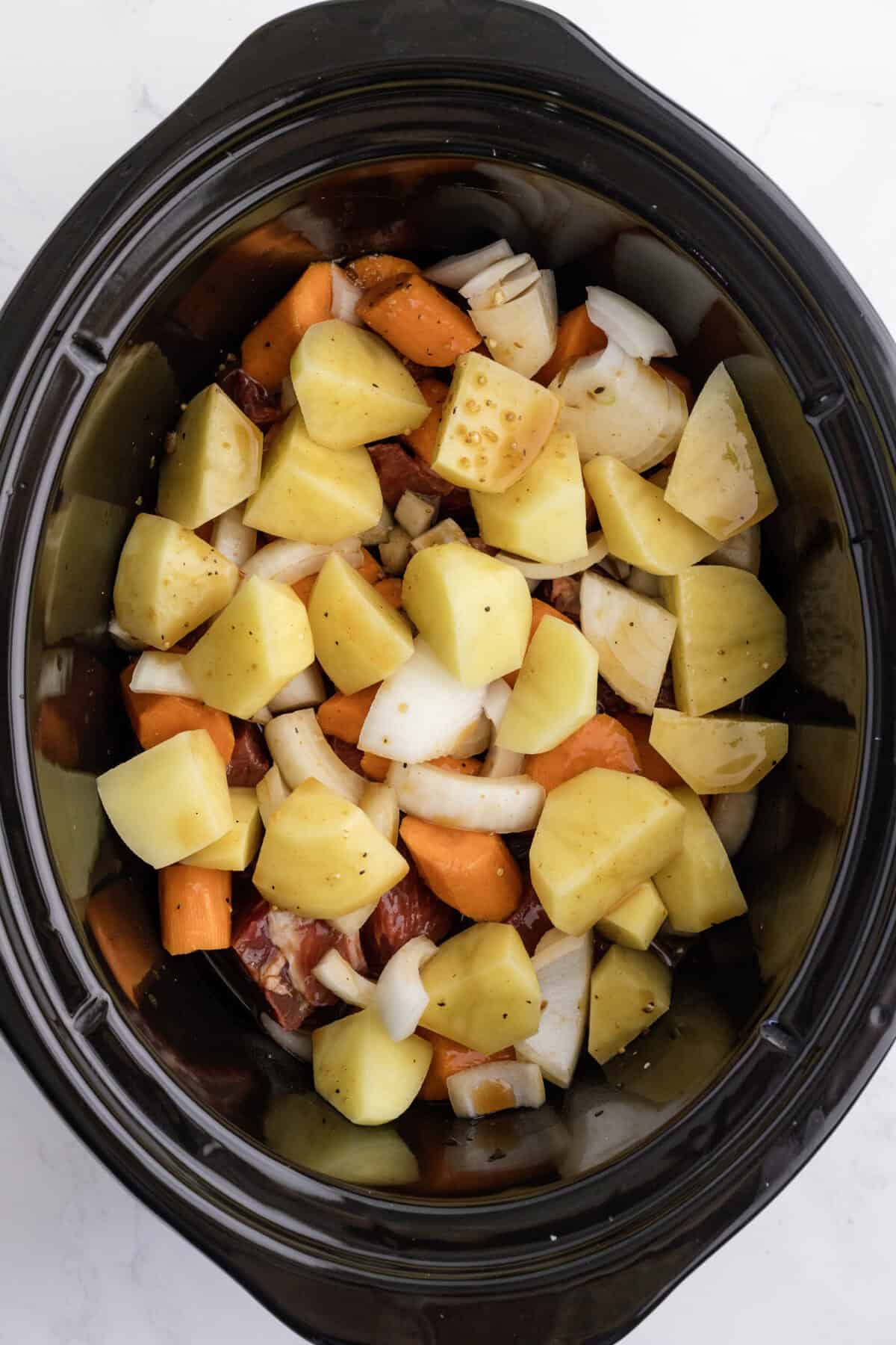 beef and veggies layered inside of a black crockpot.