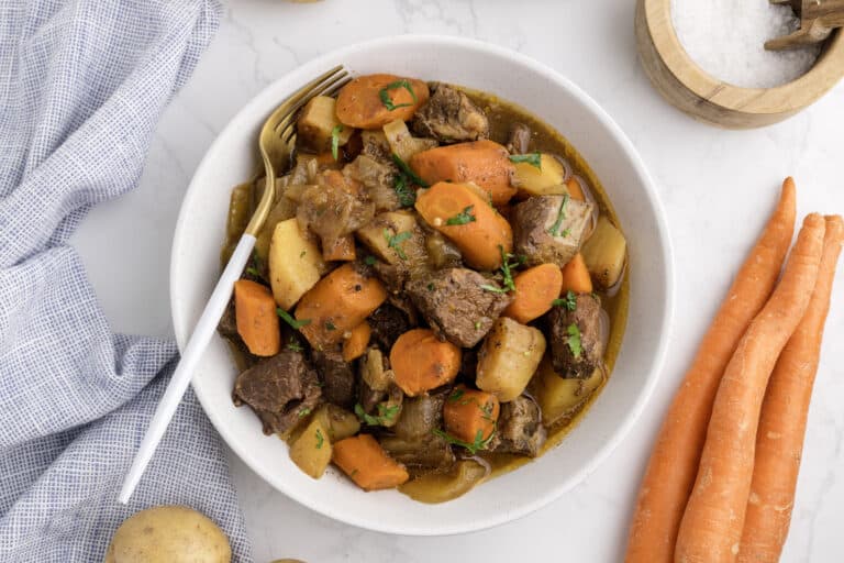 white bowl of honey balsamic beef stew with a light blue tea towel to the side.