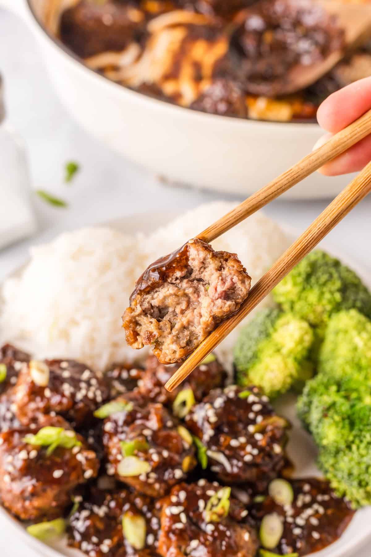 holding a Mongolian meatball with chopsticks over the plate.