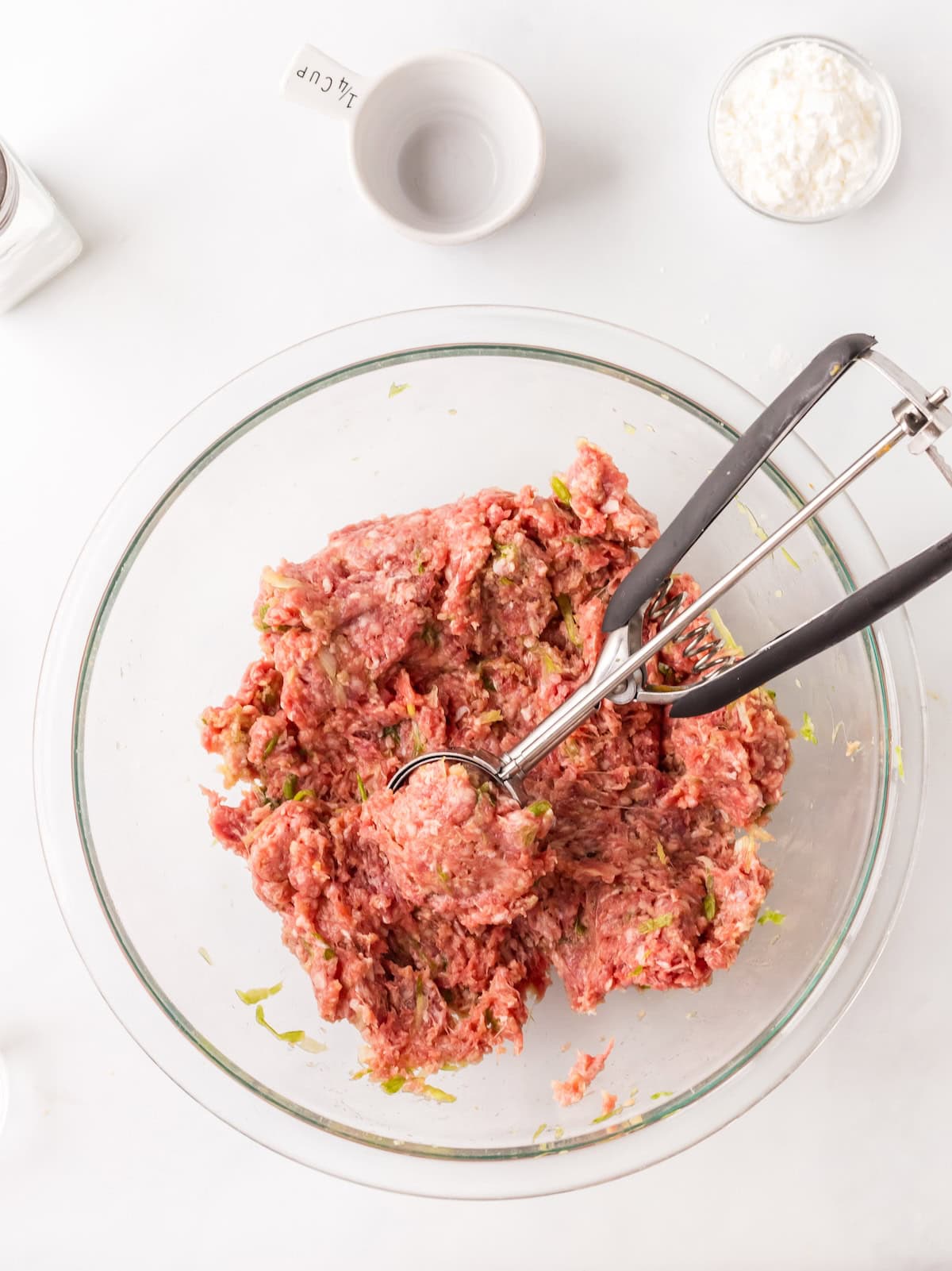using a cookie scoop to measure out the meatballs.