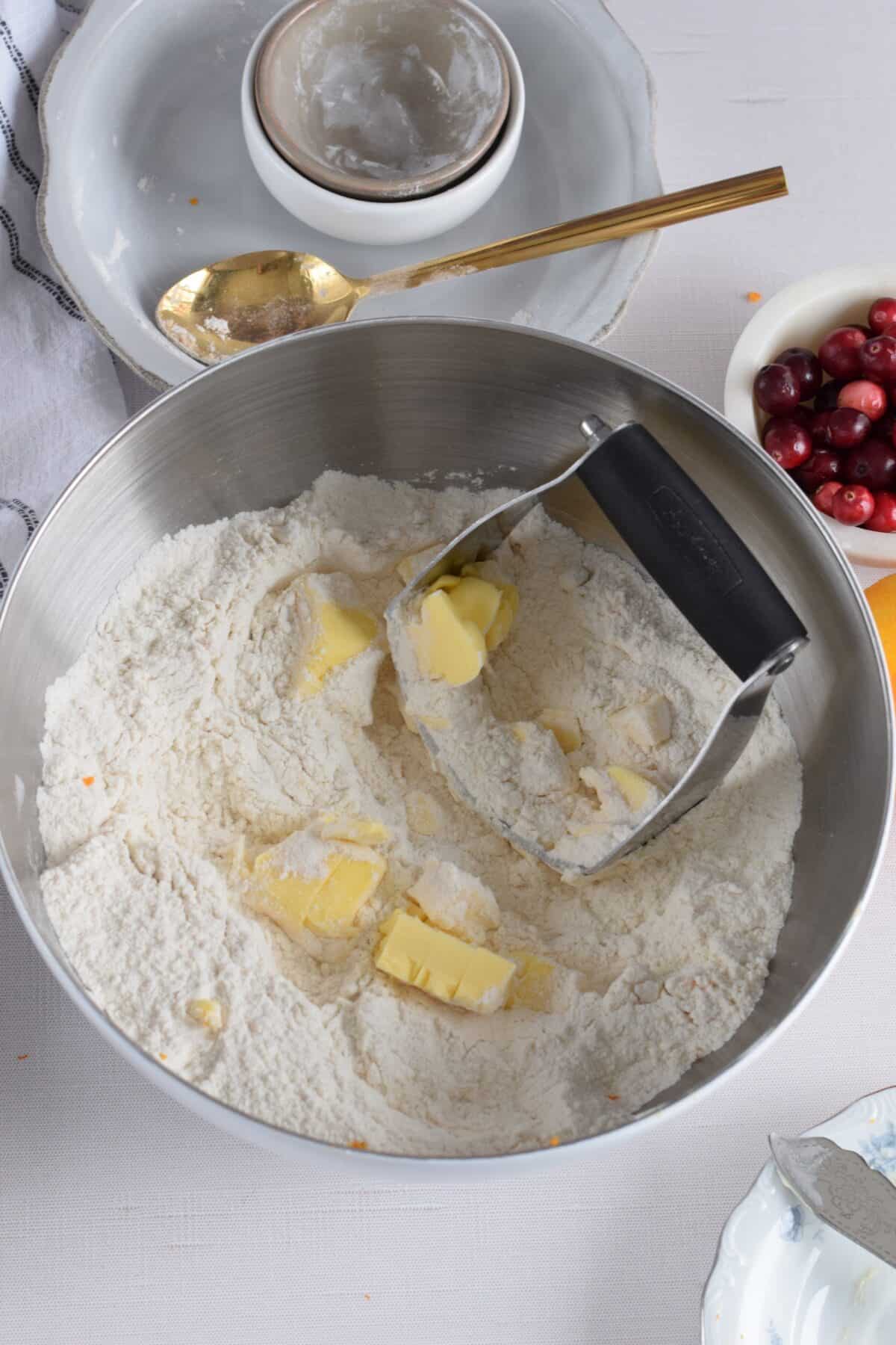 cubes of butter on top of flour mixture in a bowl with the pastry cutter inside.