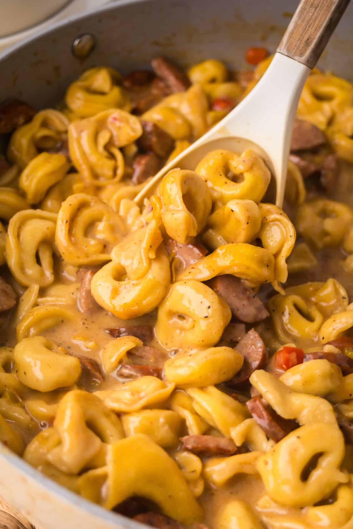 creamy cajun tortellini in a large skillet with a spoon to show the texture.