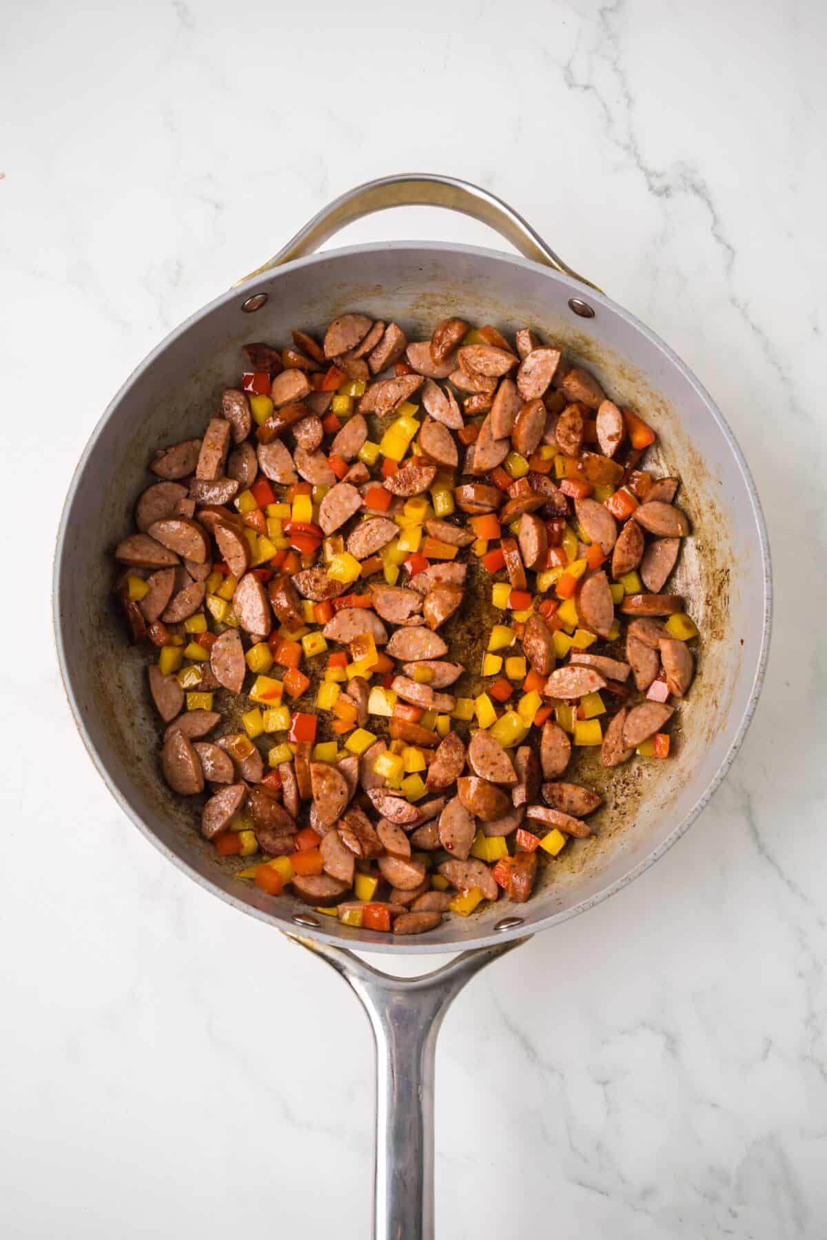 cooking sausage and bell peppers in a skillet for the creamy cajun tortellini recipe.