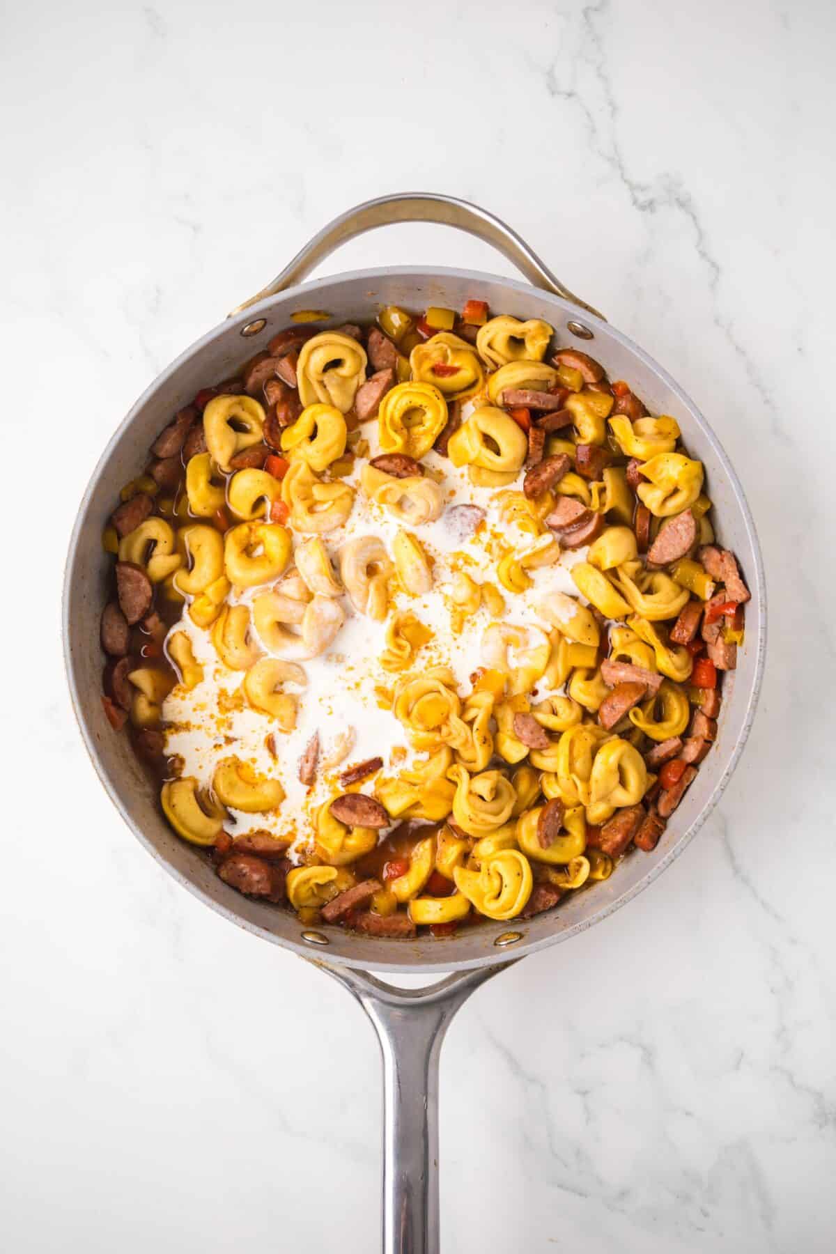 adding the creamy and seasonings with the tortellini and sausage mixture in the skillet.